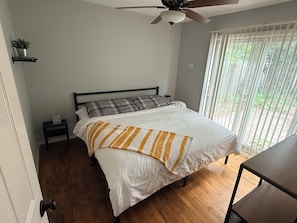 A bedroom with a bed, a ceiling fan, a window with blinds, and a small table. - Charming Vintage Home On A Quiet St (Sterling Heights)