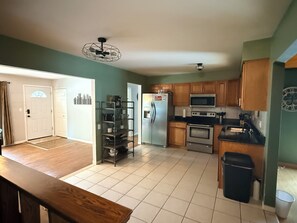 A kitchen with wooden cabinets, a stainless steel refrigerator, a microwave, and a stove. There is a ceiling fan and a trash can. - Charming Vintage Home On A Quiet St (Sterling Heights)