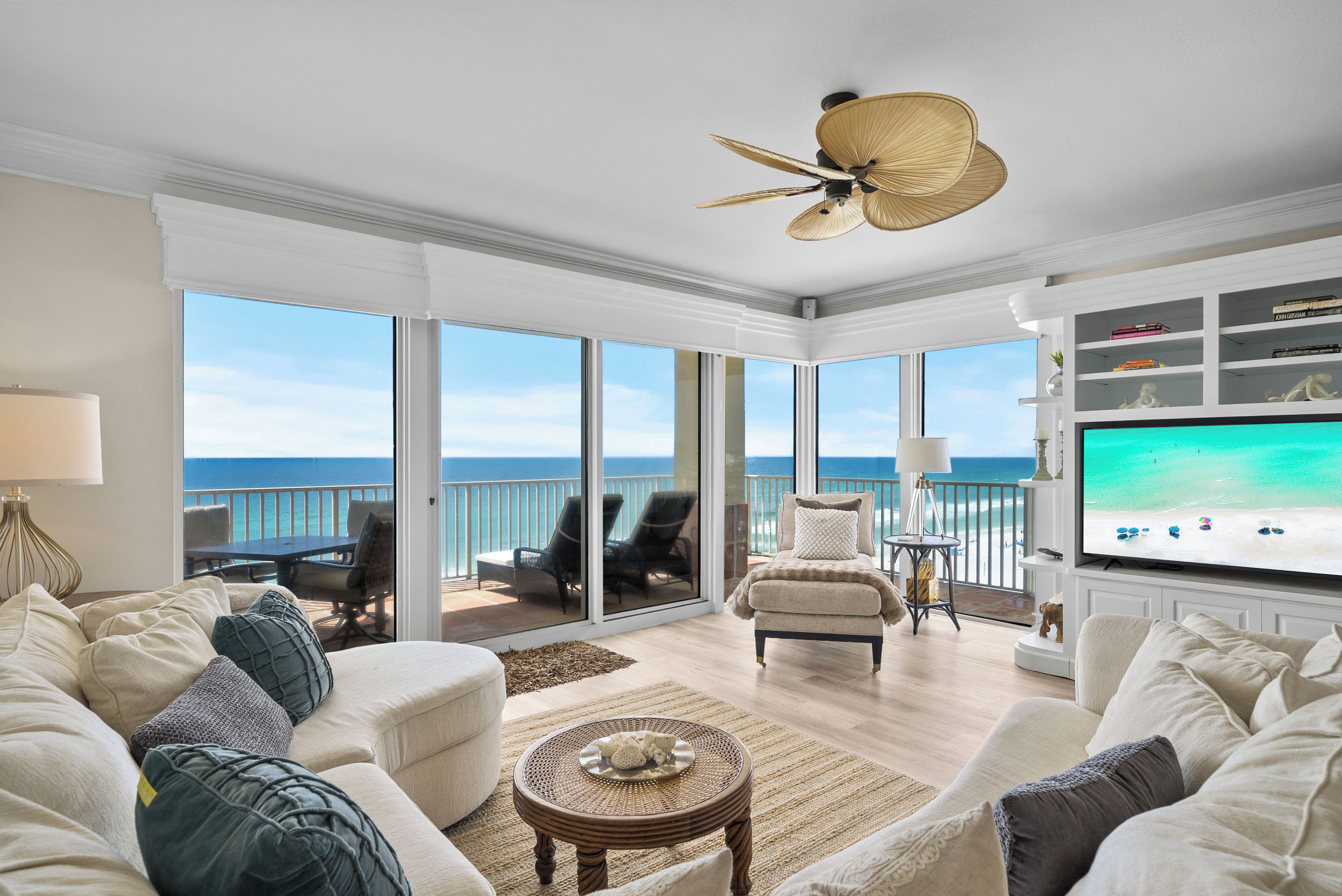 Een ruime woonkamer met een grote televisie, comfortabele zitmogelijkheden en een balkon met uitzicht op de oceaan.