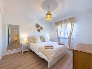 A hotel room with a bed, bedside tables, a mirror, a hanging light fixture, and a window with curtains. - Barbosa's House by ACasaDasCasas (Ericeira)