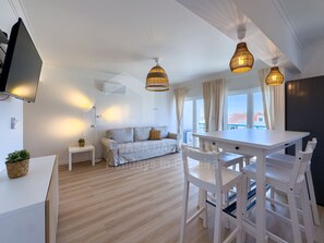 A modern living room with a sofa, a dining table with chairs, a flat-screen TV mounted on the wall, and a large window with curtains. - Barbosa's House by ACasaDasCasas (Ericeira)