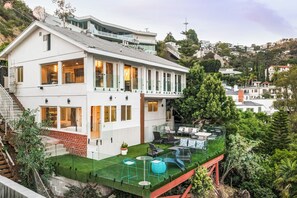 Ein modernes, zweistöckiges Haus mit Balkon, einer kleinen Terrasse mit Gartenmöbeln und Blick auf die umliegende Hügellandschaft.