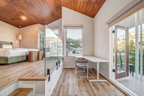 Ein modernes Schlafzimmer mit Bett, Nachttischen, einem Schreibtisch und einem großen Fenster mit Blick auf die Stadt.