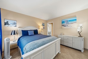 A bedroom with a bed, bedside tables, a dresser, and artwork on the walls. - Anchors Away - Pacific Grove Condo - Your Oceanfront Beach Pad (Pacific Grove)