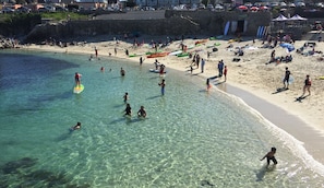 Een strand met helder water, mensen aan het zwemmen en paddleboarden, en boten aan de kust.