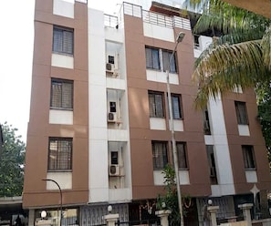 A multi-story residential building with balconies, air conditioning units, and a gated entrance. - Suite Room Tathawade (Paud)
