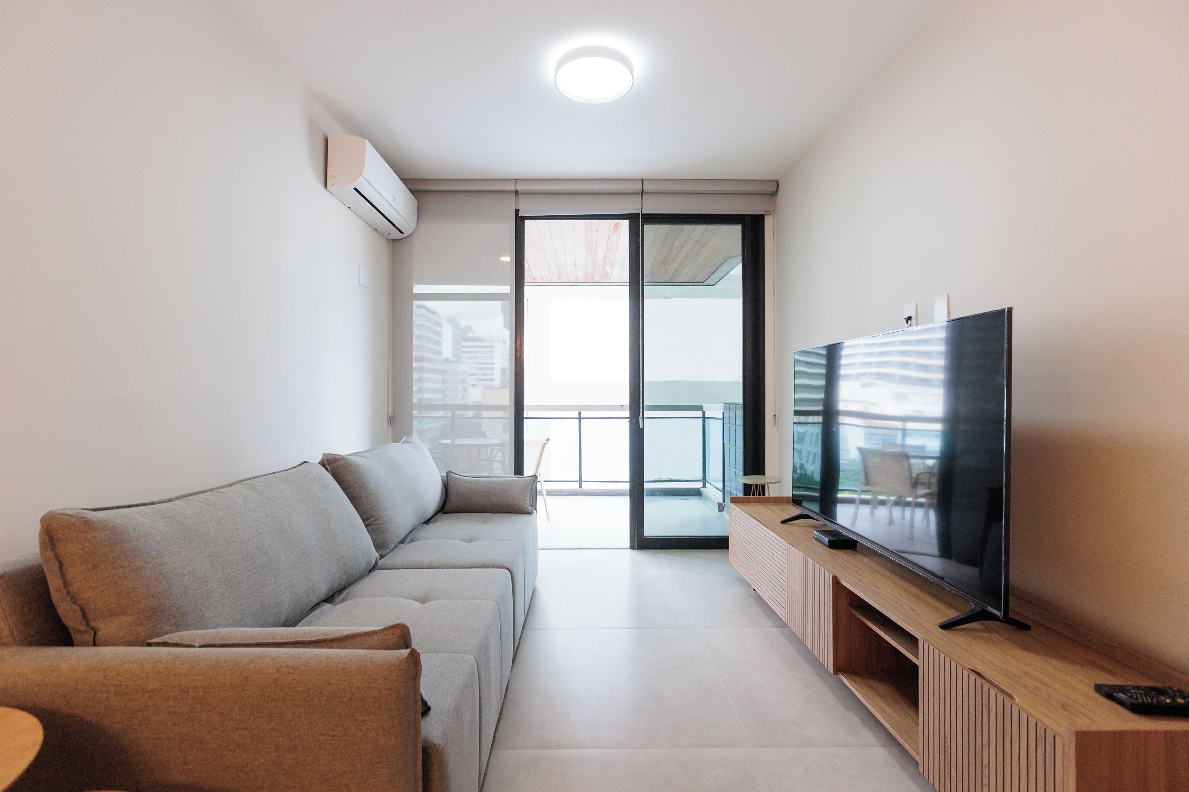 Un salon moderne avec un canapé d’angle, un téléviseur à écran plat et un balcon offrant une vue agréable.