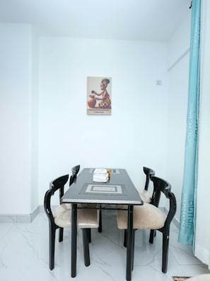 Ein Essbereich mit Tisch und vier Stühlen, einem Bild an der Wand und einem blauen Vorhang.