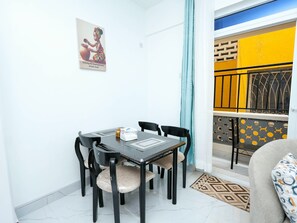 A dining area with a table and chairs, a poster on the wall, and a view of a balcony with yellow and black decor. - Soothing spacios 1-bedroom apartment in charming Bamburi near the beach, (Bamburi)
