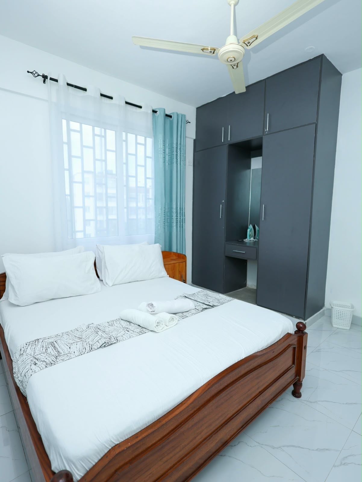 Ein Schlafzimmer mit Bett, Kleiderschrank, Deckenventilator und einem Fenster mit Vorhängen.