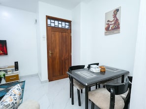 A dining area with a wooden door, a table with chairs, a television, and a framed picture on the wall. - Soothing spacios 1-bedroom apartment in charming Bamburi near the beach, (Bamburi)