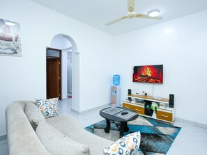 A living room with a sofa, coffee table, and a painting of a fire on the wall. - Soothing spacios 1-bedroom apartment in charming Bamburi near the beach, (Bamburi)