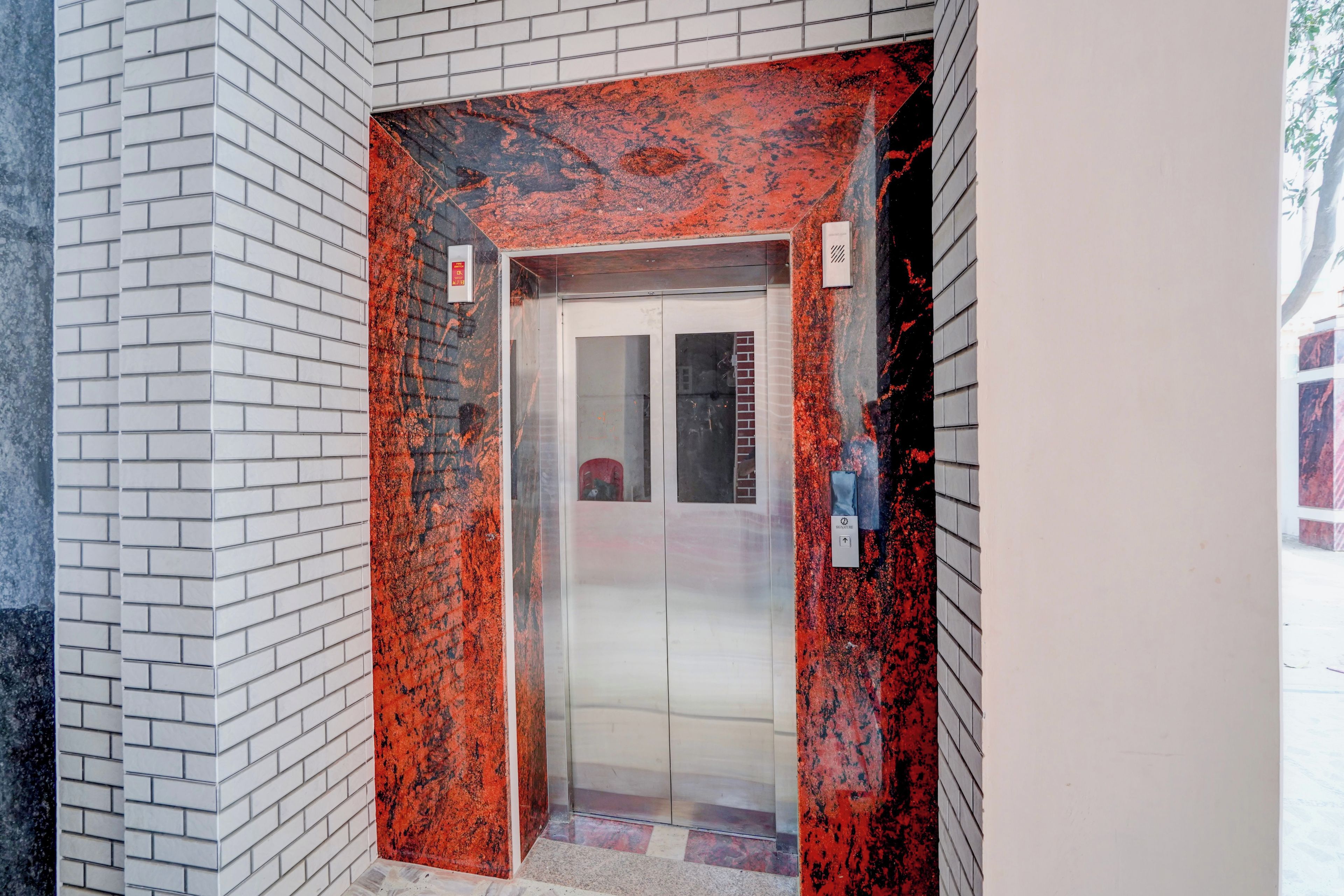 An elevator with a red and black marble finish, white tiled walls, and a glass door.