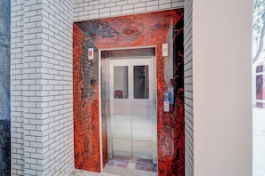 Un ascensor amb acabat de marbre vermell i negre, parets de rajola blanca i una porta de vidre.