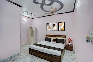 A bedroom with a bed, a ceiling fan, a nightstand, a vase with flowers, and framed artwork on the wall.