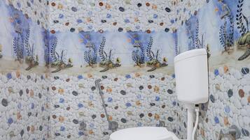 A bathroom with a white toilet, a shower, and walls covered in pebble-like tiles.