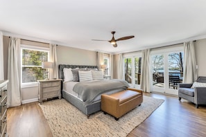 Une chambre à coucher avec un grand lit, une table de chevet, une commode et une vue sur l’extérieur grâce à de grandes fenêtres.