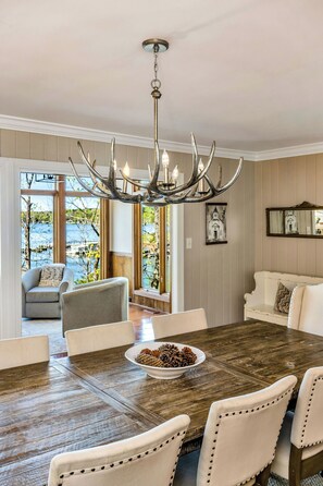 Une salle à manger avec une grande table en bois, des chaises à revêtement blanc et un lustre orné de motifs métalliques évoquant des bois de cerf.