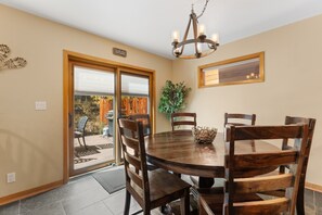 A dining area with a round table, six chairs, a chandelier, a sliding glass door, and a sign that reads 'PLEASE HOLD YOUR HORSES'. - Spacious 5BR Wildernest Home | Private Hot Tub & Views (Silverthorne)
