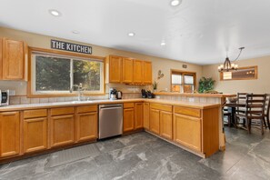 A modern kitchen with wooden cabinets, a built-in dishwasher, and a large window. - Spacious 5BR Wildernest Home | Private Hot Tub & Views (Silverthorne)