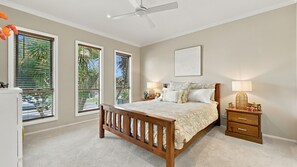 A bedroom with a bed, bedside tables, a ceiling fan, and large windows with blinds. - Your Perfect Inverloch Getaway (Inverloch)