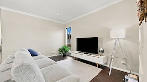 A modern living room with a flat-screen TV, a white sofa, a floor lamp, and a potted plant. - Your Perfect Inverloch Getaway (Inverloch)