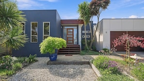 A modern two-story house with a blue exterior, a front door with a glass panel, and a driveway leading to a garage. - Your Perfect Inverloch Getaway (Inverloch)