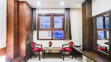 A hotel room with a large window, a desk, two chairs, a small table, and a mirror.