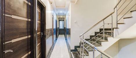 A hotel hallway with a marble floor, a staircase with metal railings, and wooden doors with a number plate.