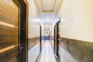 A corridor with wooden doors on one side and marble walls on the other, leading to a hallway with doors at the end. - Super Collection O Sindhi Camp (Jaipur)