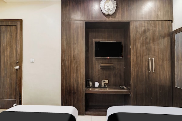 Habitación de hotel con dos camas, un armario de madera con televisión y una pequeña estantería con hervidor y otros objetos.