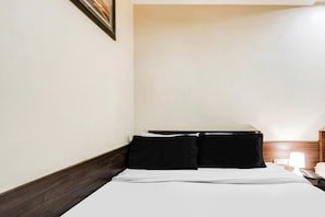 Habitación de hotel con una cama, dos almohadas negras, un cabecero de madera, una mesita de noche con una lámpara y un cuadro en la pared.