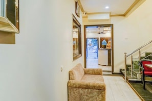A hallway with a sofa, a staircase, and a door leading to a room with a ceiling fan. - Super Collection O Sindhi Camp (Jaipur)