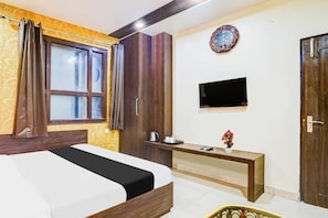 Quarto de hotel com cama, escrivaninha, televisão de tela plana, relógio na parede e porta.