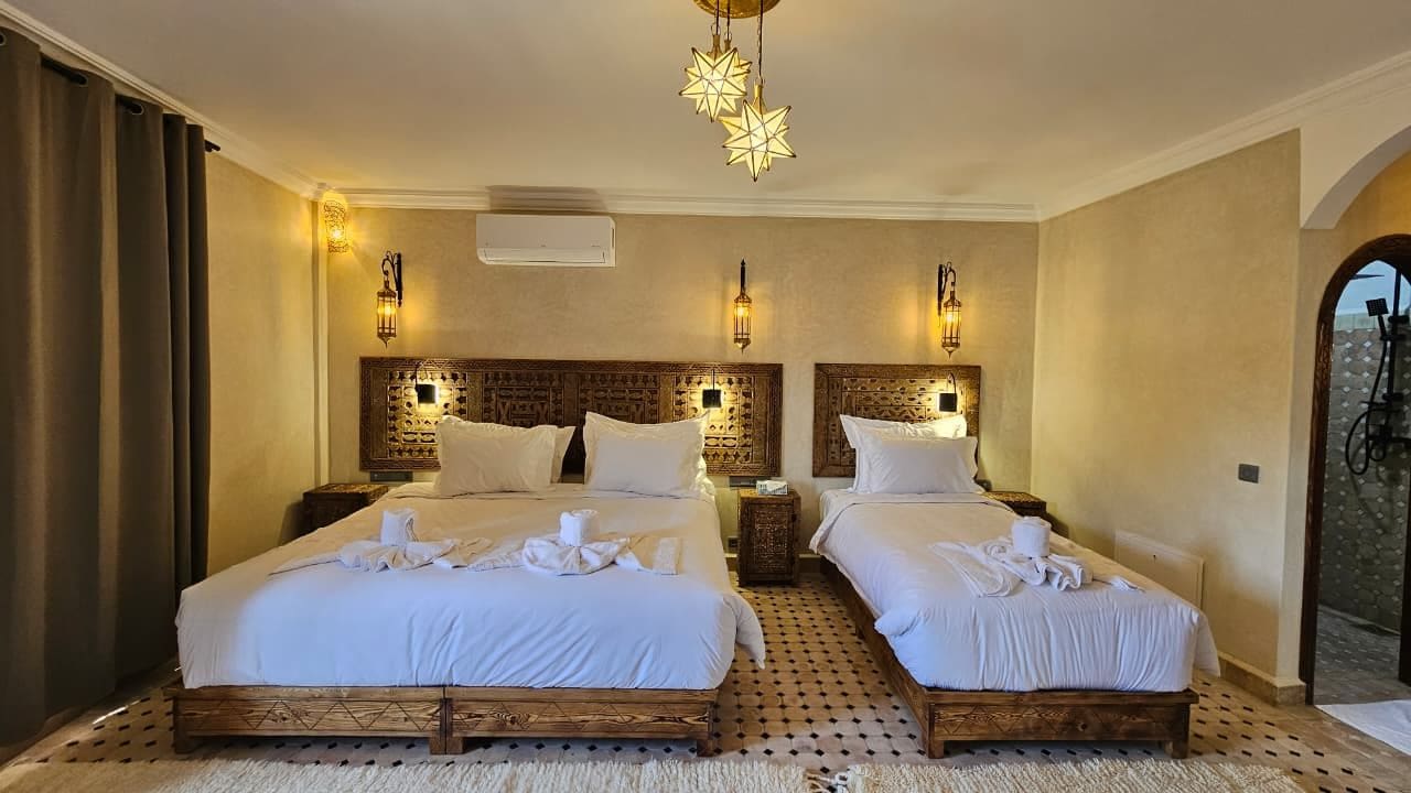 Ein Hotelzimmer mit zwei Betten, einem gemusterten Kopfteil, Wandleuchten und einer Deckenlampe.