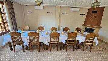 A dining room with a long table set for 12, wooden chairs, and a fireplace.
