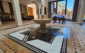 A lobby with a tiled fountain, seating area, and a view through a glass door.