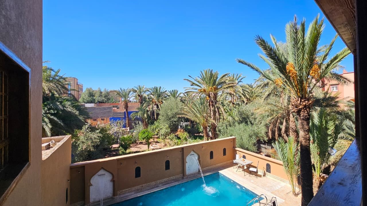 A pool with a water feature, surrounded by palm trees and a clear blue sky.