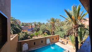 Zwembad met een fontein, omgeven door palmbomen en een helderblauwe lucht.