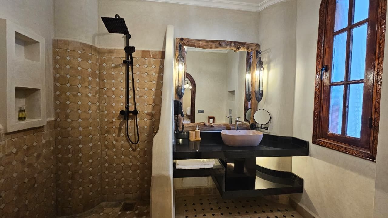 Un baño con pared de diseño de piedra, un espejo grande, un lavabo con pileta de cobre y una ducha con cabezal de ducha manual.