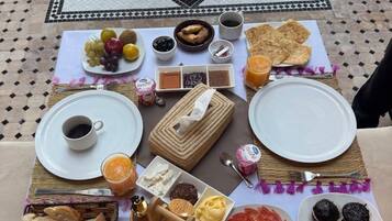 A table set with a variety of foods and drinks, including bread, fruits, and condiments, on a tiled floor with a decorative pattern.