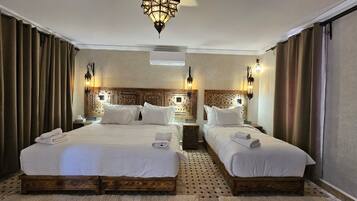 A hotel room with two beds, a patterned headboard, wall-mounted lamps, and a ceiling light fixture.