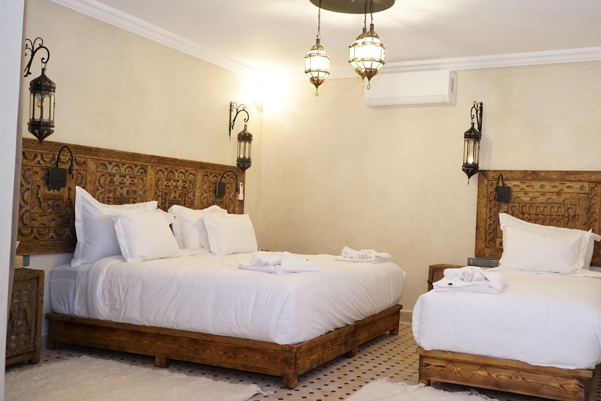 Una cama doble con cabecera de madera y dos mesitas de noche, cada una con una lámpara de pared.