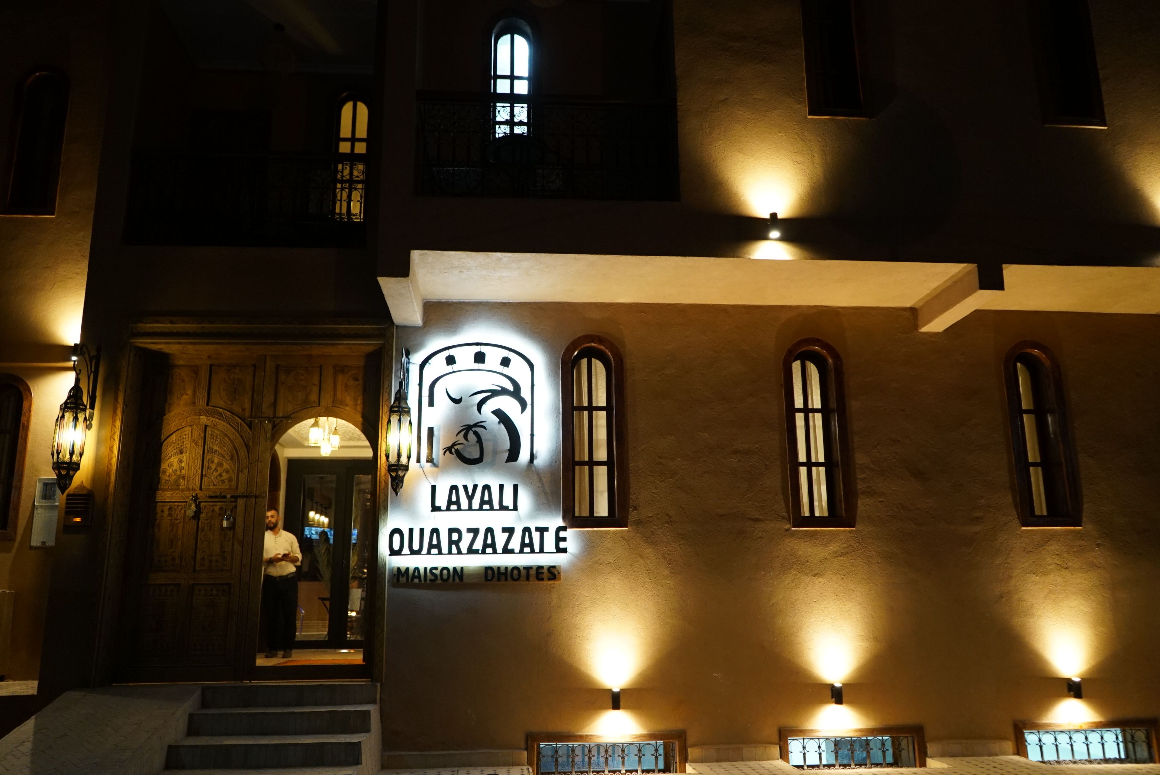 A building facade with illuminated signage for 'Layali Quarzazate Maison Photos.'
