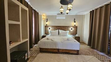 A hotel room with a large bed, a headboard with decorative panels, bedside lamps, and a small bedside table.