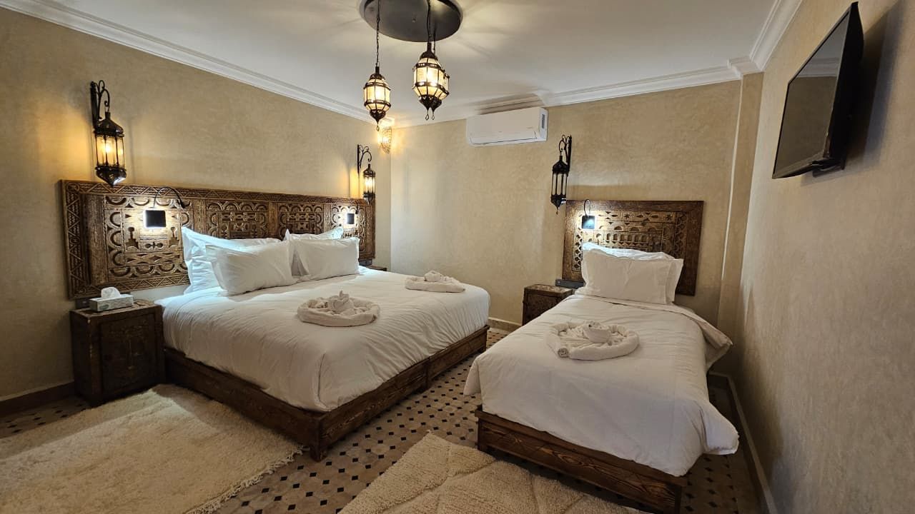 Habitación de hotel con dos camas, cada una con cabecero de madera, ropa de cama blanca y apliques decorativos en la pared.