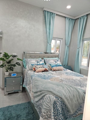 A bedroom with a bed, a nightstand, a potted plant, and a window with curtains. - The Ocean Whisper's Escape @Jett's Place (Mt. Thompson)