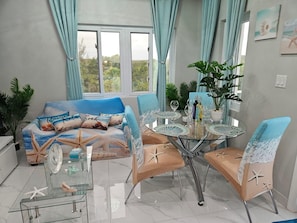 A room with a sofa bed featuring a sea-themed design, a glass dining table with chairs, and a potted plant. - The Ocean Whisper's Escape @Jett's Place (Mt. Thompson)