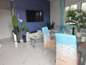 A dining area with a blue wall, a flat-screen TV, and a table set for two with a beach-themed table runner. - The Ocean Whisper's Escape @Jett's Place (Mt. Thompson)