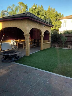 Eine Terrasse mit Grill, Gartenmöbeln und einem gepflegten Rasen.